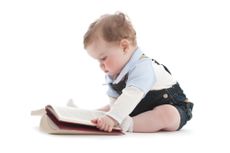 A baby sits looking at a book.