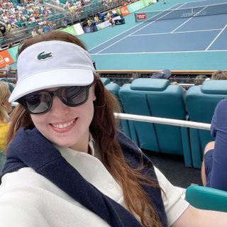 a woman wears a Lacoste tennis visor and white polo shirt