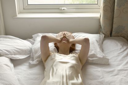 woman lays in bed with her hands over her eyes