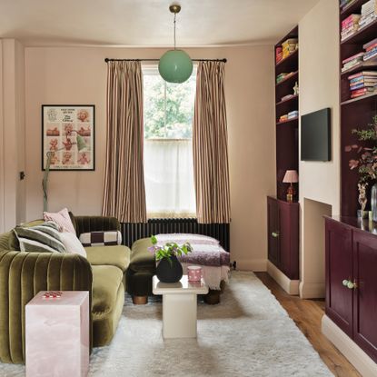 a small living room with a green velvet sofa and dark burgundy fitted alcove shelving and cabinetry