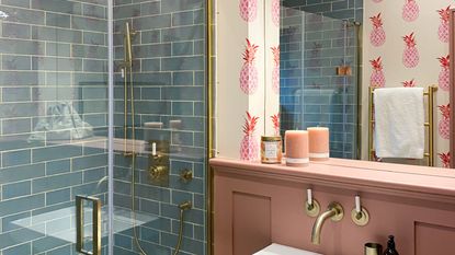 Learning how to make a shower room look bigger is always useful. Here is a shower room with blue tiles, pink pineapple wallpaper, and a white sink on a pink wall