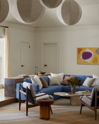 Image of a white living room with a blue sectional sofa. There are multiple paper lanterns hanging in the center of the room. There are white and brown pillows on the sofa.