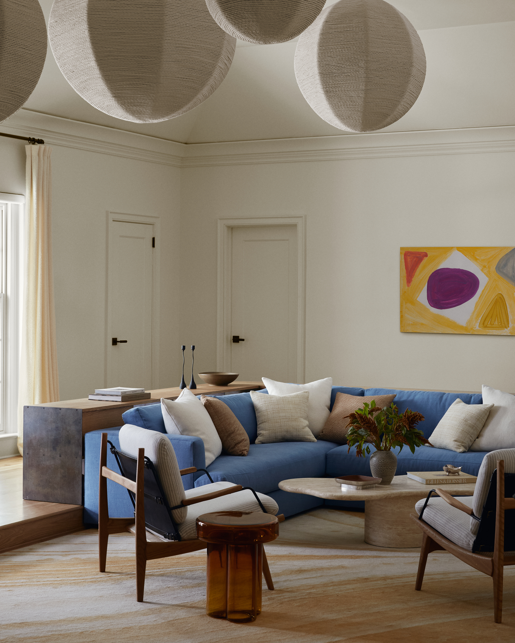 Image of a white living room with a blue cuttingof. Several paper lanterns hang in the middle of the room. There are white and brown pillows on the sofa.