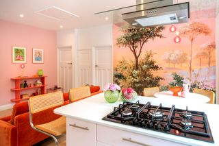The kitchen-diner has a fully pink wall with a tree mural on the other whilst the kitchen cupboards are pink