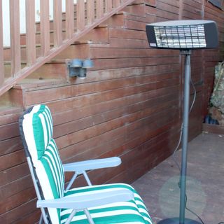 The Devola Core 2kW Freestanding Patio Heater next to a green and white striped chair on wooden decking