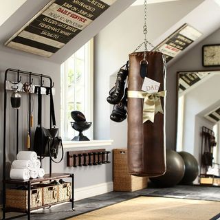 industrial home gym with a punchbag, a hanging rail with towels and a bag, and a giant ball on the tile floor