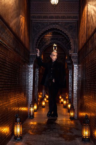 Serge Lutens standing in an alley way with dozens of lanterns on the floor illuminating the area.