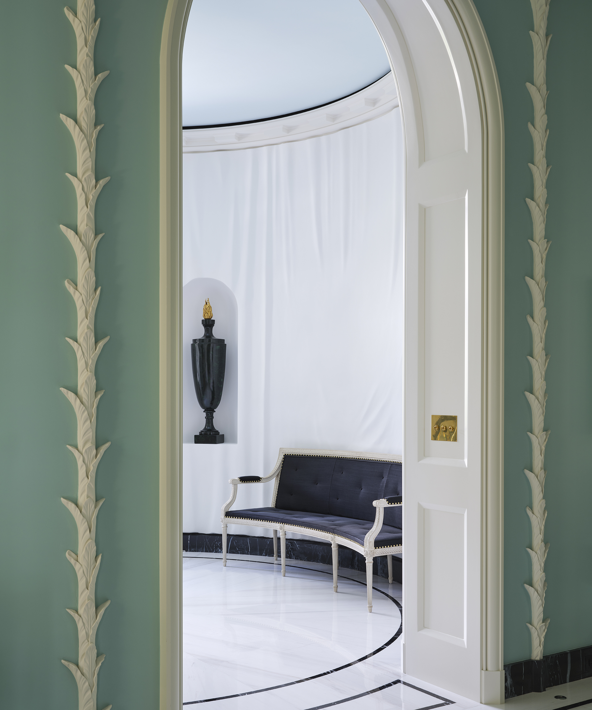 white curved entryway with a blue sofa in it and a vase in a niche in the wall