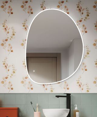 A blob mirror on a floral patterned wall above a sink