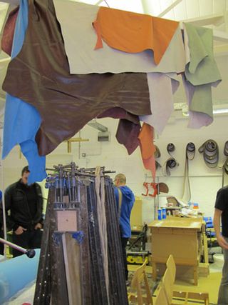 Colourful hides handing from the rafters in a workshop with people in the background