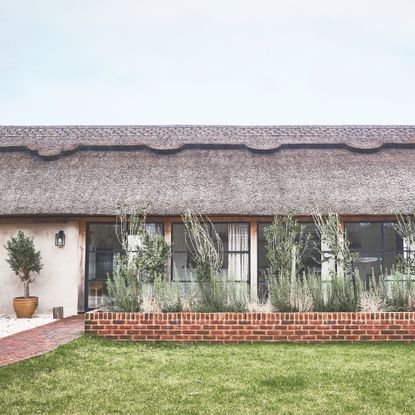 exterior of thatched barn conversion with Crittall windows and low brick wall in front with planting