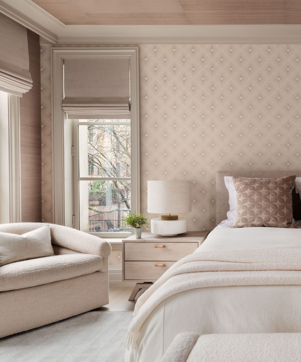 A light pink bedroom with geometric wallpaper and a boucle armchair