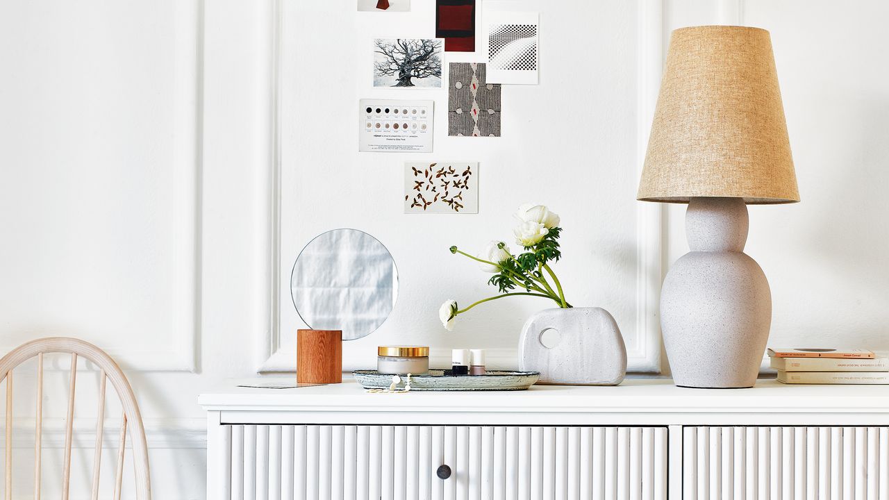 White chest of drawers with mirror, table lamp and artwork