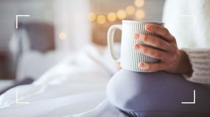 Woman holding a mug of tea sitting down on bed about to go to sleep with fairy lights in the background, representing drinks that help you lose weight