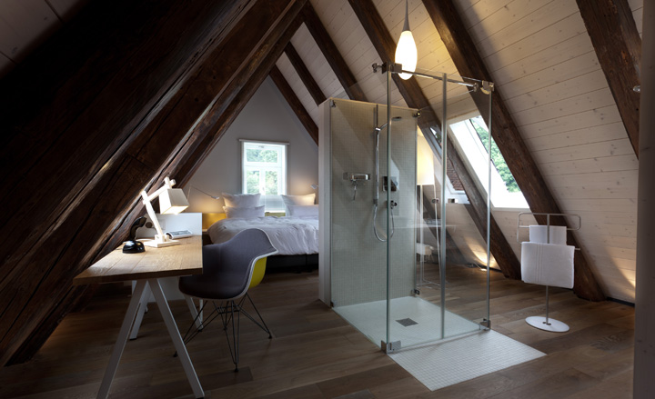 Bedroom, bed with desk, chair and lamp, shower in centre of room with overhead light fixture