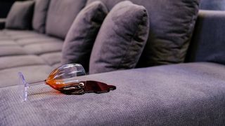 Red wine and glass knocked over on sofa