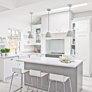A white kitchen with three small pendant lights above an island with white bar stools