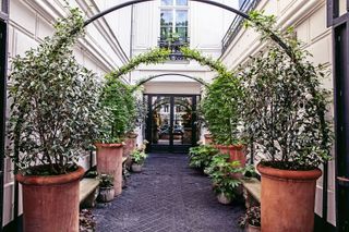 A grand hotel entrance with terracotta planters each side and arched canopy with climbing plants
