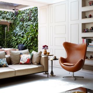 Living room with leather sofa and armchair below long skylight with foliage wall in the background