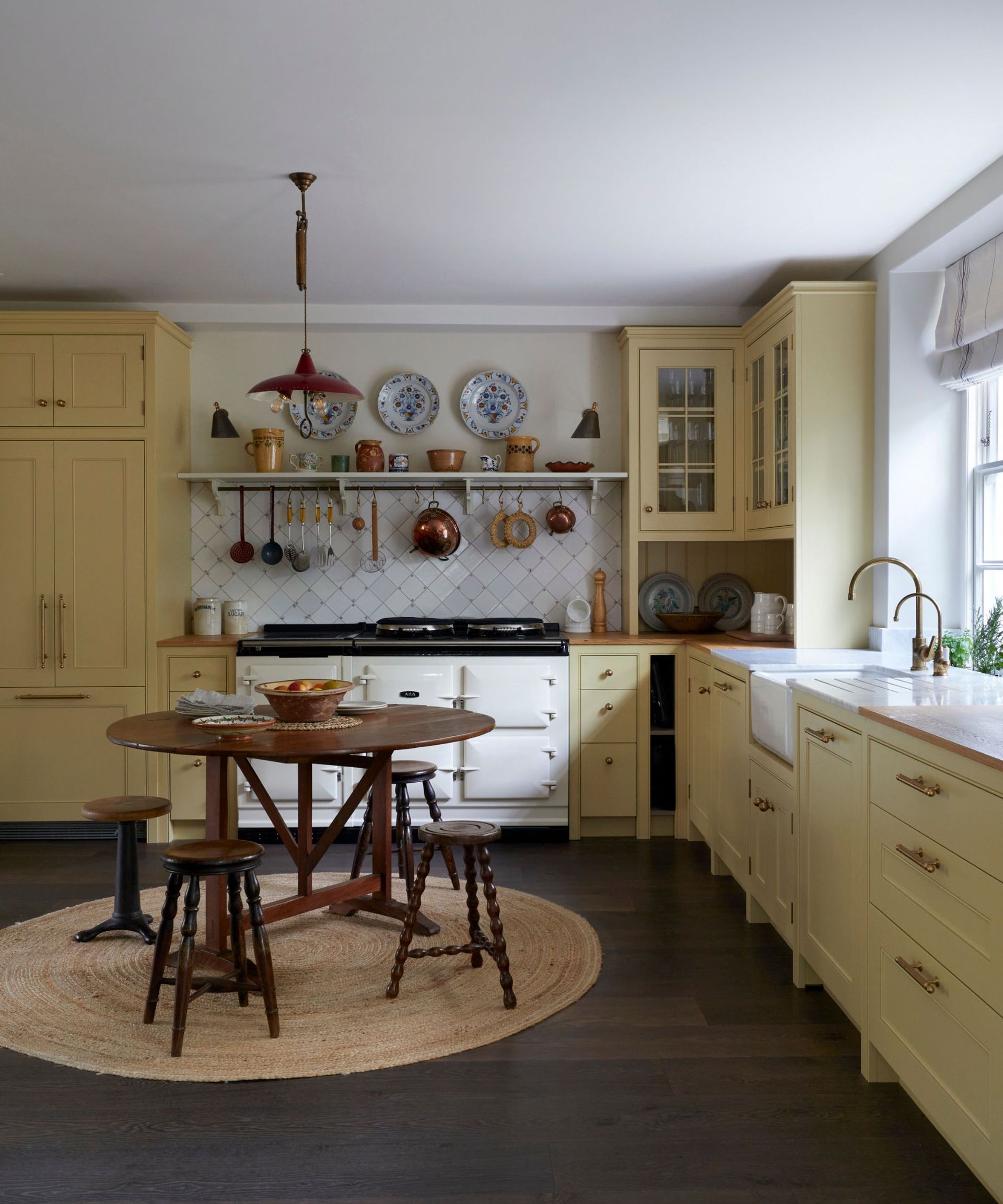 A midimalist kitchen with yellow cabinets, a traditional white aga, and blue and white plates hung on the wall