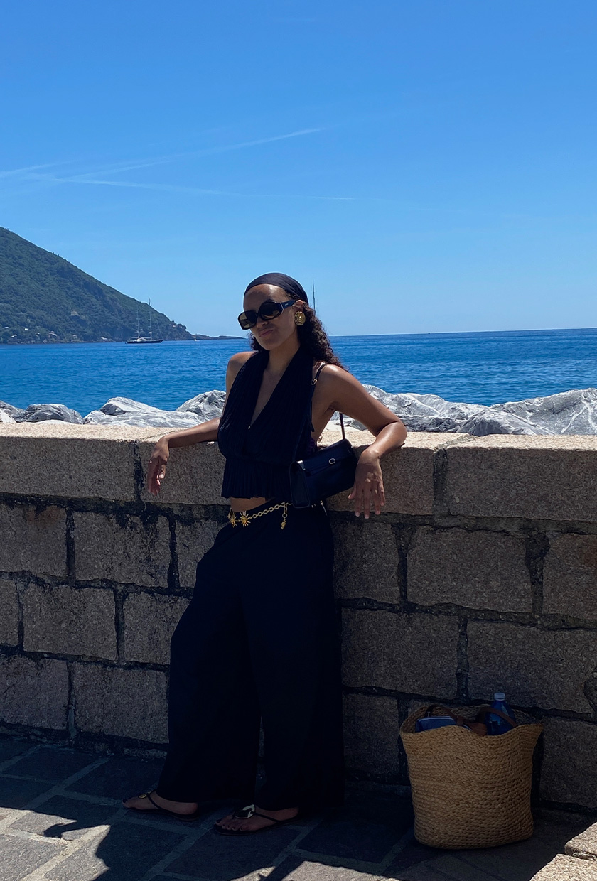How to pack for Italy is shown in a picture of a fashion editor wearing a black headscarf, black halter, black linen pants, and black flip flops