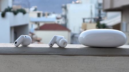 The Huawei FreeBuds Neo buds and case on a ledge, in front of a city.