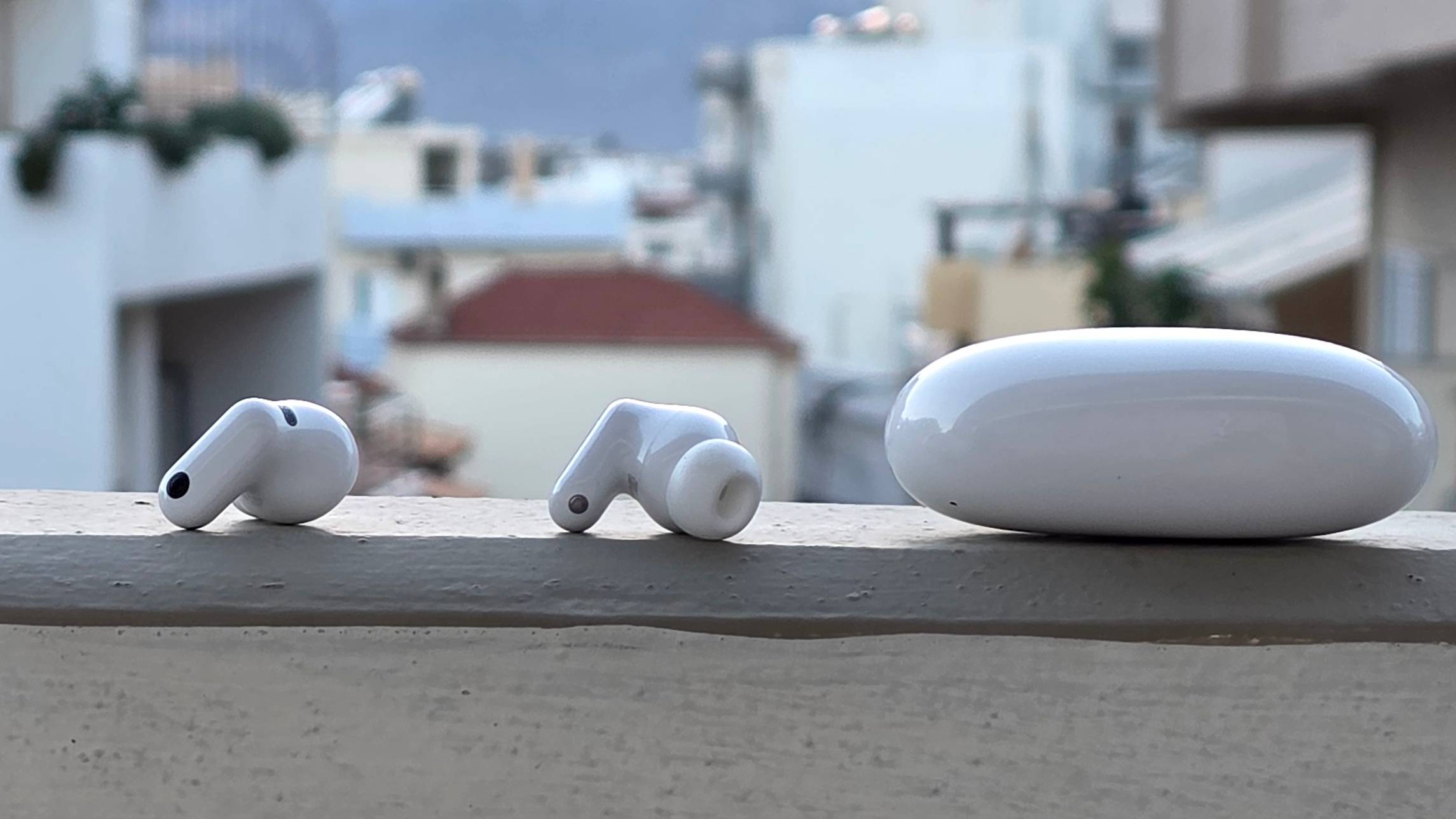 The Huawei FreeBuds Neo buds and case on a ledge, in front of a city.