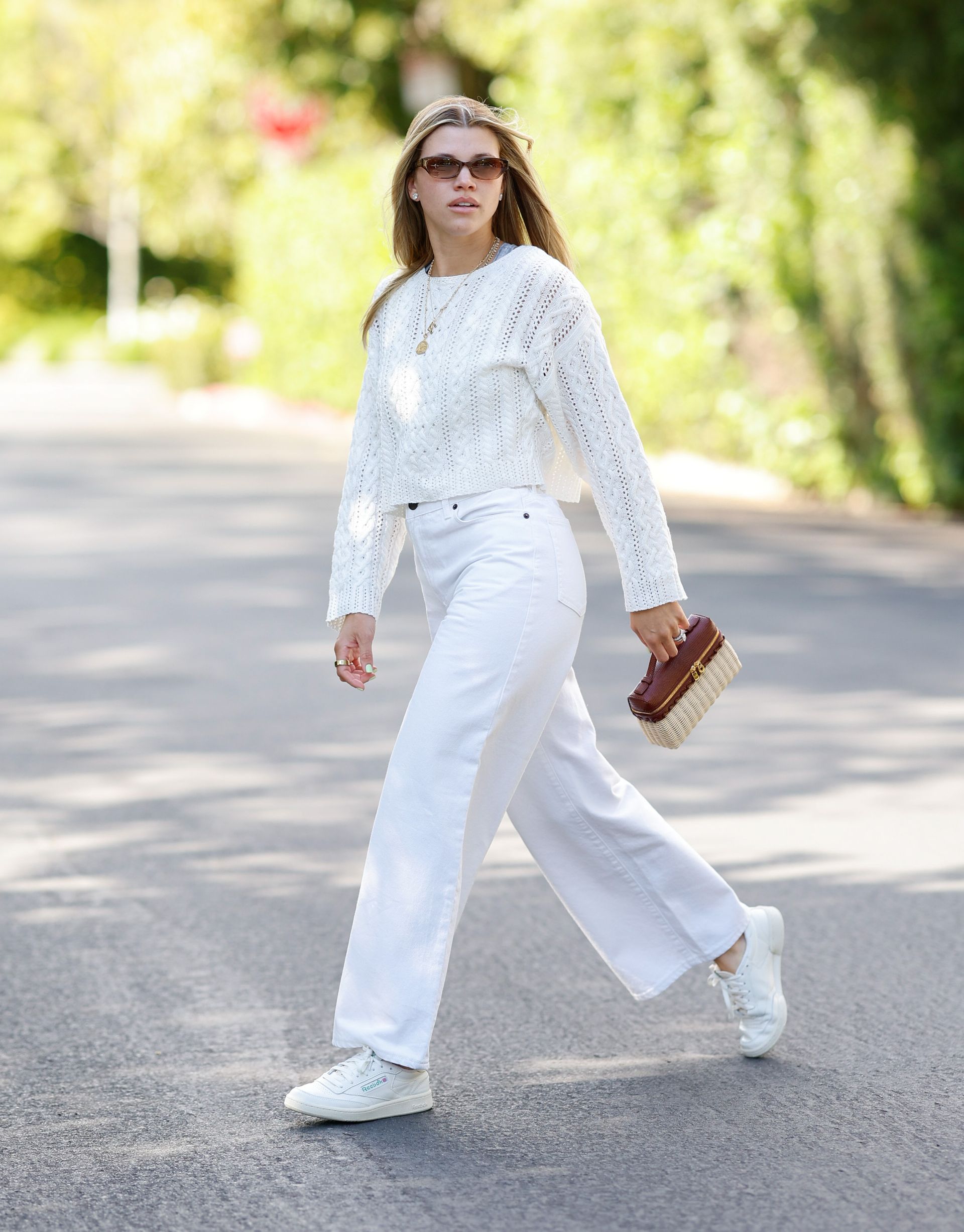 Sofia Richie wears a white sweater, white jeans, and white sneakers.