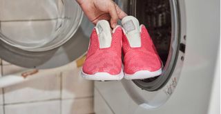 person putting trainers into a washing machine but experts say you should not put shoes in a washing machine
