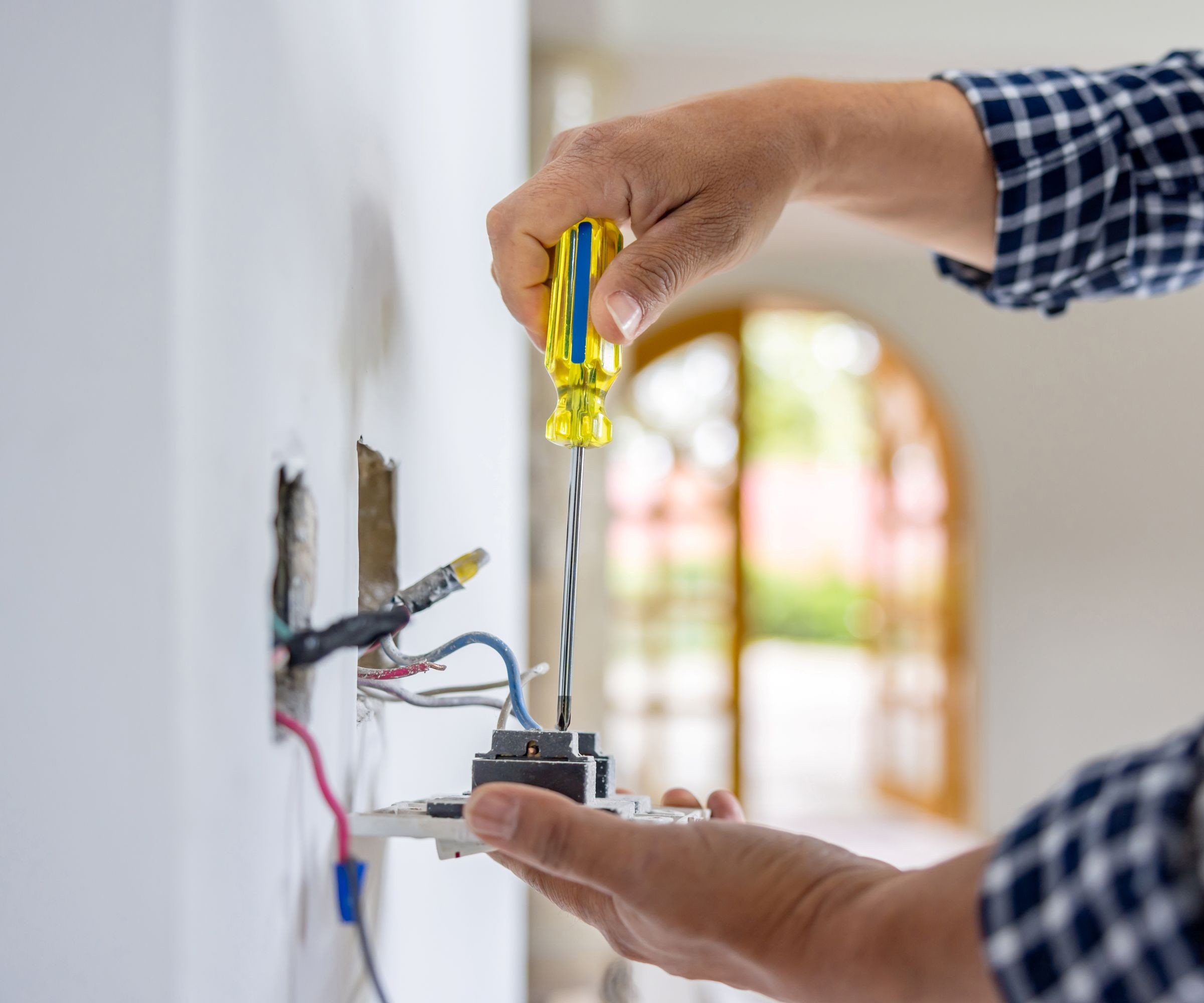 A man with a yellow handled screwdriver wiring a plug socket
