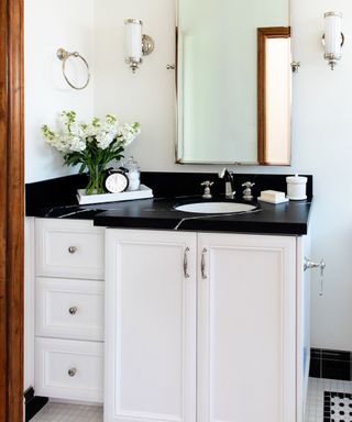 A white bathroom with a white and black sink and wooden door frame
