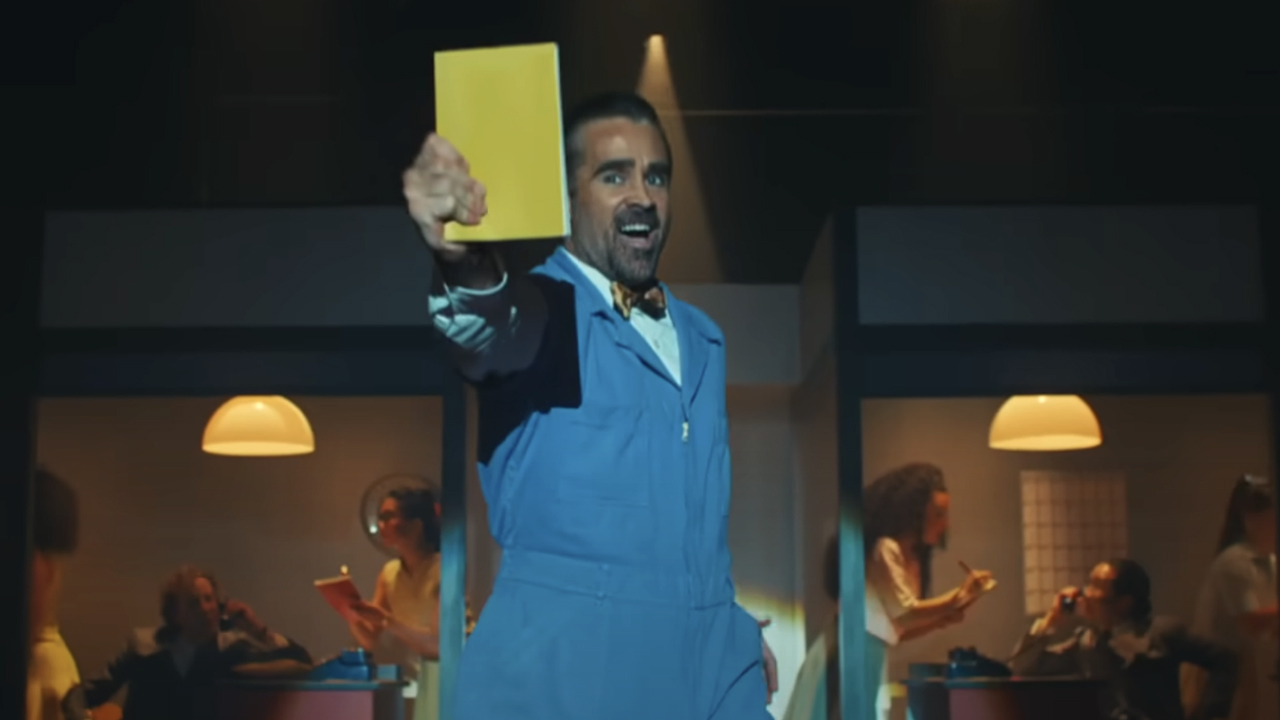 Colin Farrell in a blue jumpsuit, bow tie, and holding a book out proudly as he sings and dances in 2025's A Big Bold Beautiful Journey.
