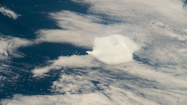 a white clump of iceberg sits below wispy clouds