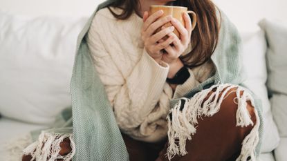 Woman sitting on the sofa with blanket, representing being contagious with a cold