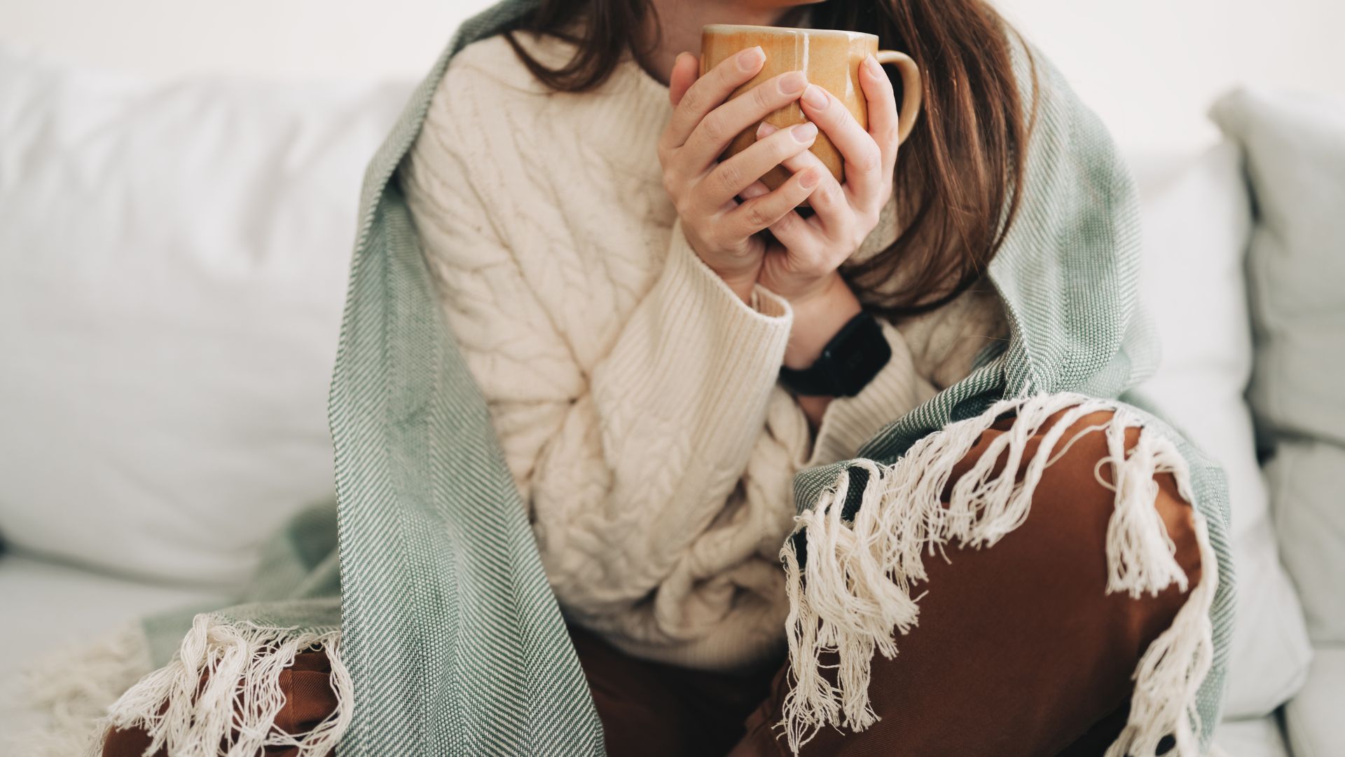 Woman sitting on the sofa with blanket, representing being contagious with a cold