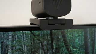 A webcam sitting on top of a black Philips Evnia 25M2N3200W monitor sitting on a wooden desk