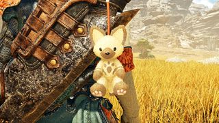 A felyne plushy hanging from a hunter's greatsword in Monster Hunter Wilds.