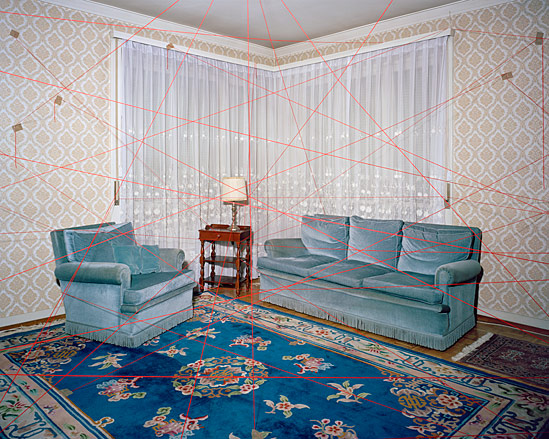 A lounge area with a blue sofa, a blue chair, a wooden coffee table, a blue patterned rug and red string crisscrossing the room.
