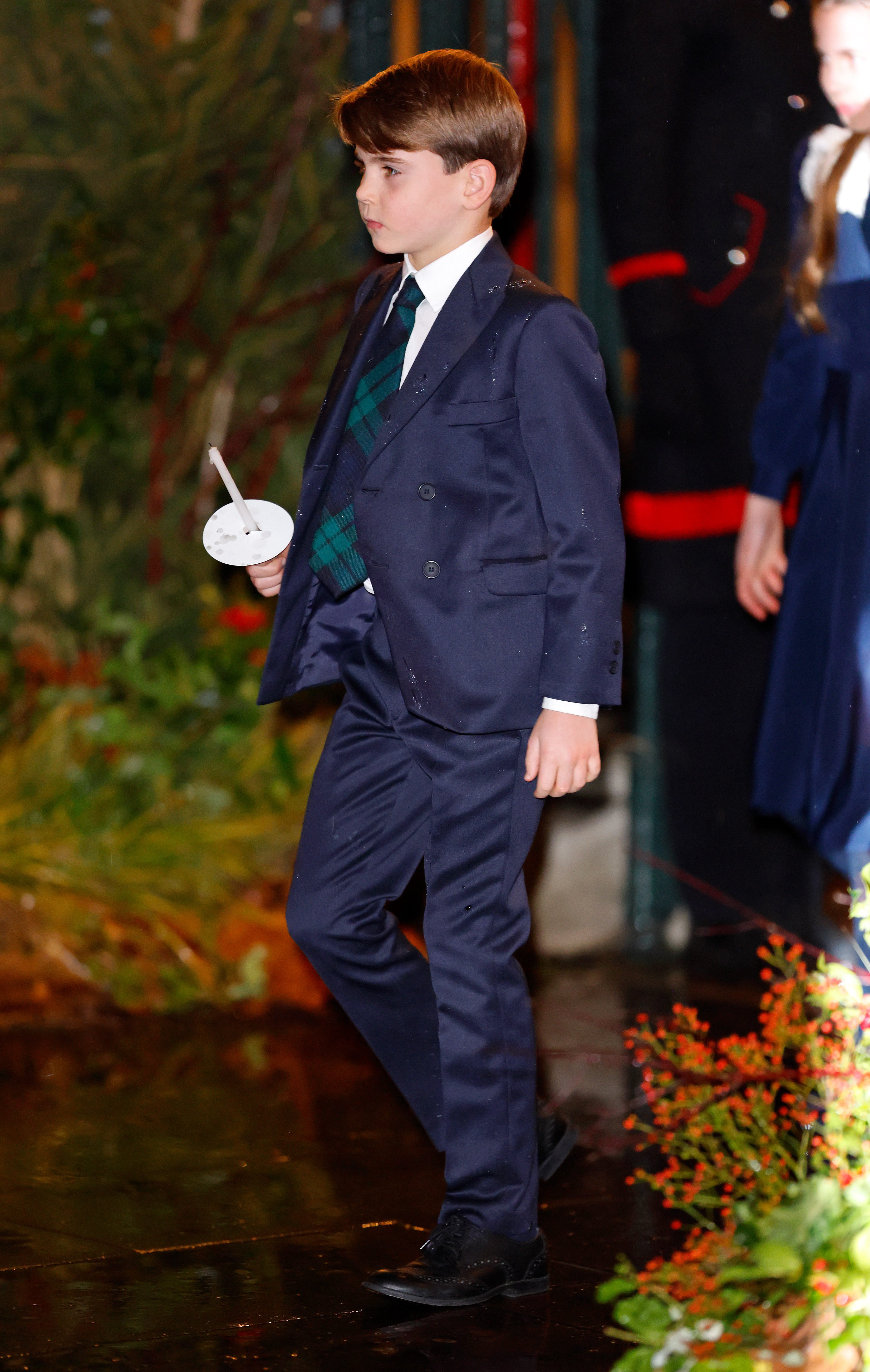 Prince Louis wearing a blue suit and black watch plaid tie holding a candle at Together at Christmas concert 2025