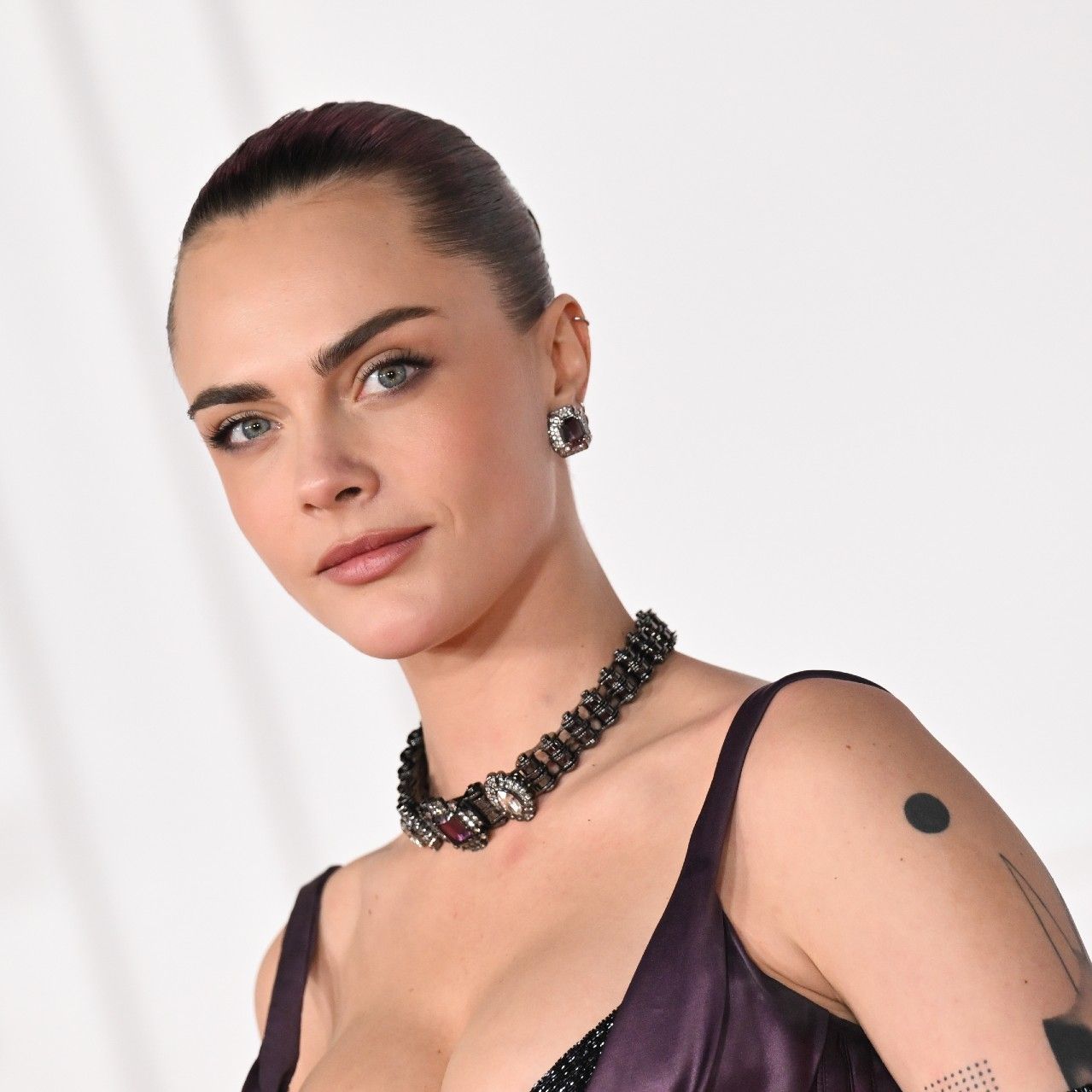 a white woman with dark hair poses for paparazzi in front of a white backdrop