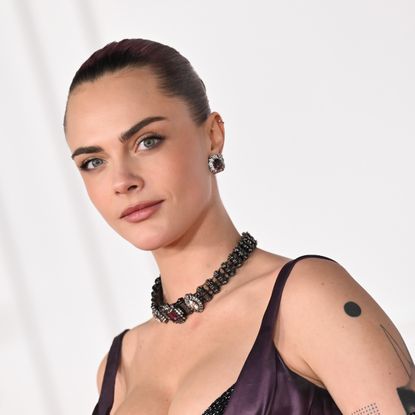 a white woman with dark hair poses for paparazzi in front of a white backdrop