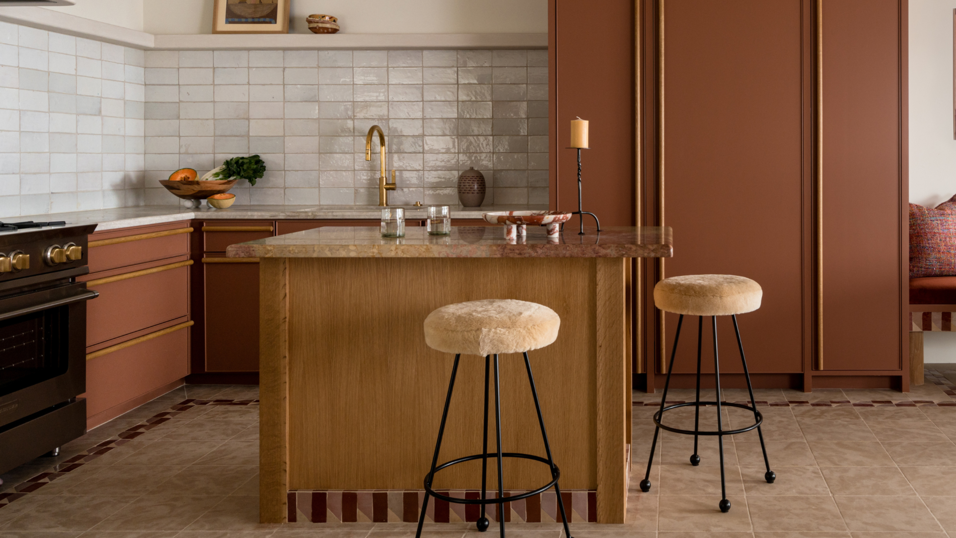 A warm muted terracotta kitchen in a modern traditional style with high ceilings and exposed beams, built in banquette seating and a striped accent for areas like the plinth.