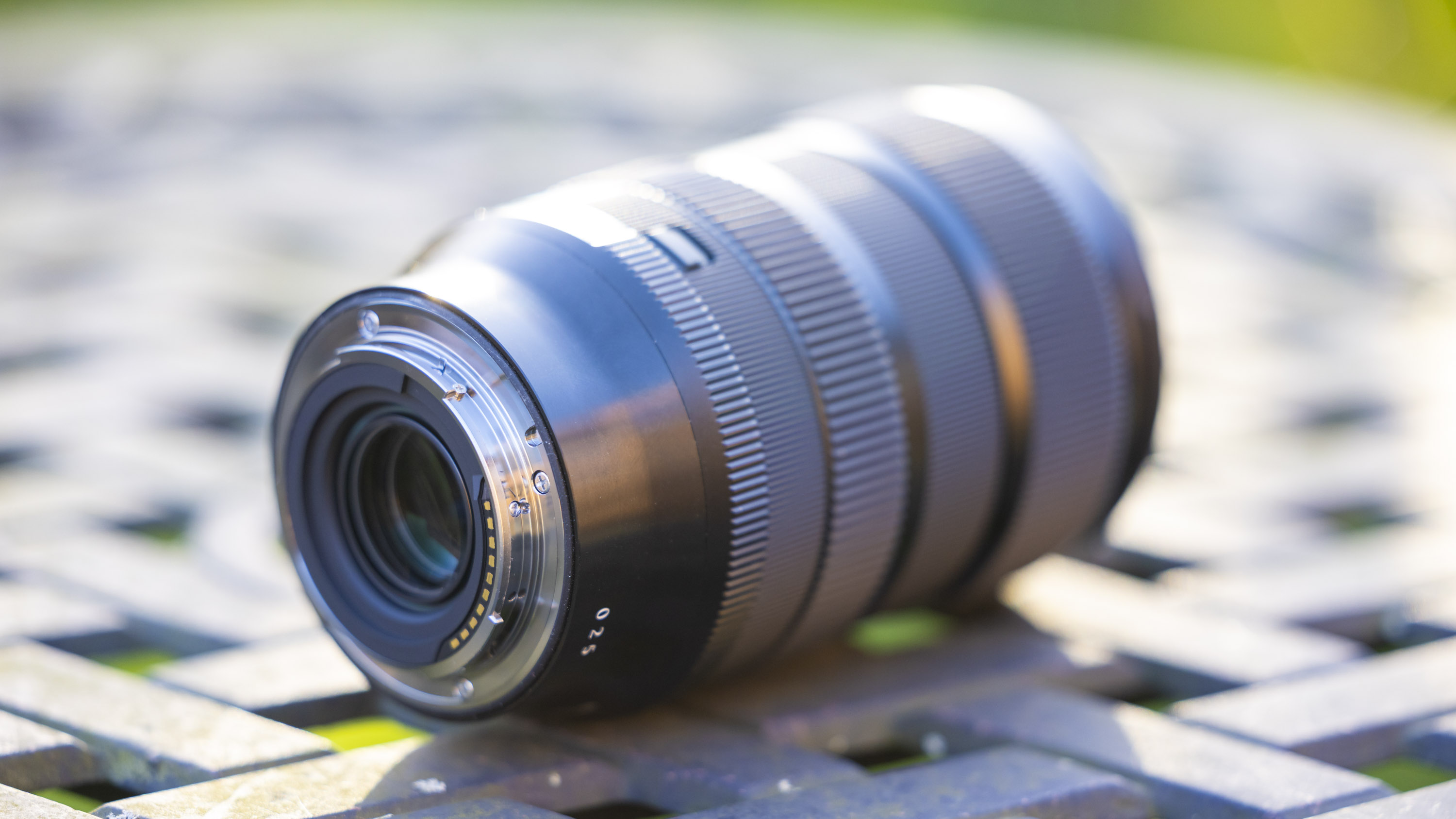 Sigma 17-40mm f1.8 DC Art lens product shot taken outdoors on a metal garden table with blurry bokeh background