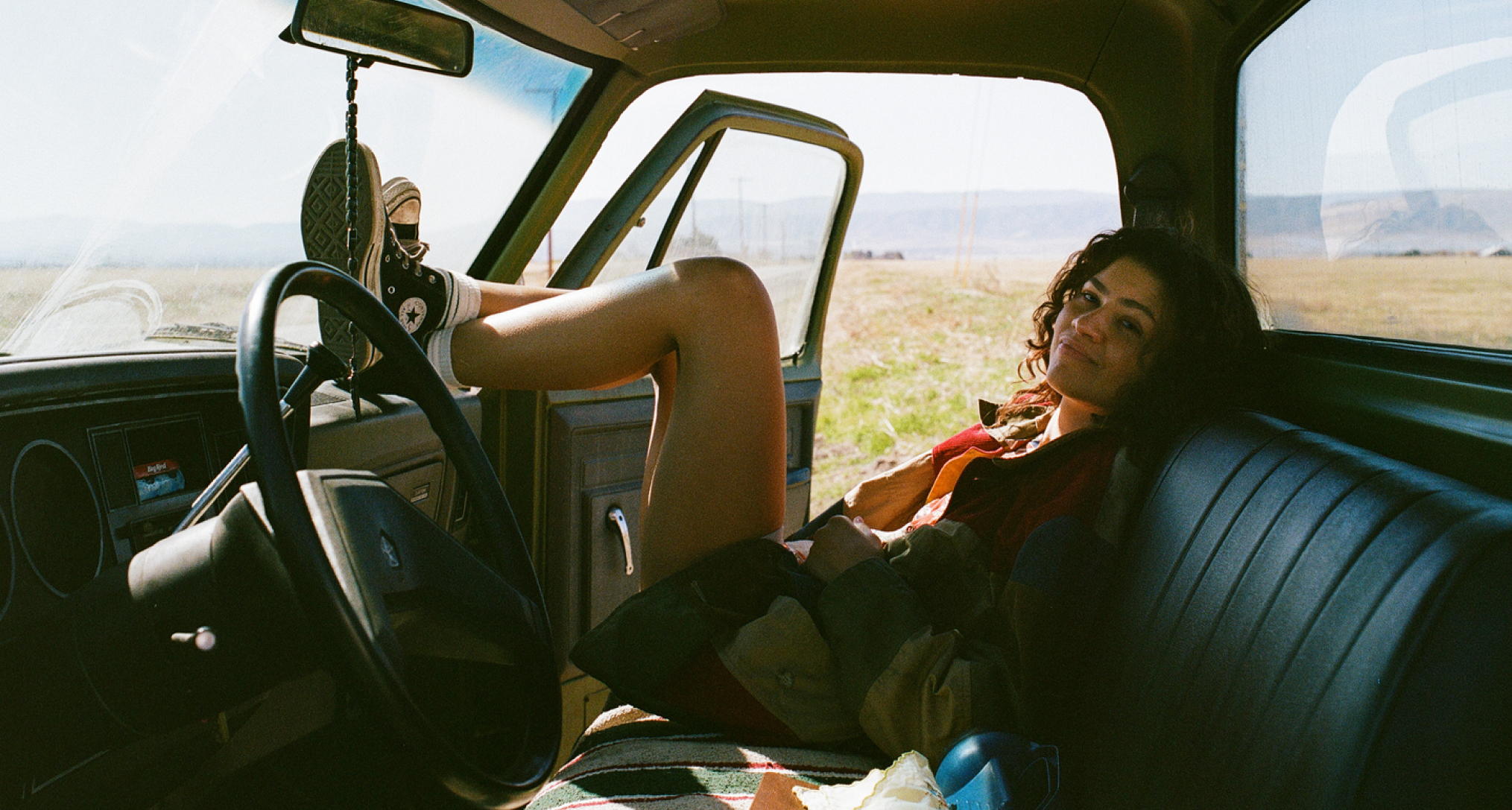 zendaya as rue laying in the passenger seat of an old looking guitar with the door open as it sits in the desert in a still from euphoria season 3