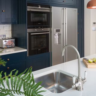 kitchen with blue cabinets silver refrigerator wash basin and white countertop