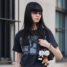A woman wears a black graphic t-shirt with bag charms on her bag.