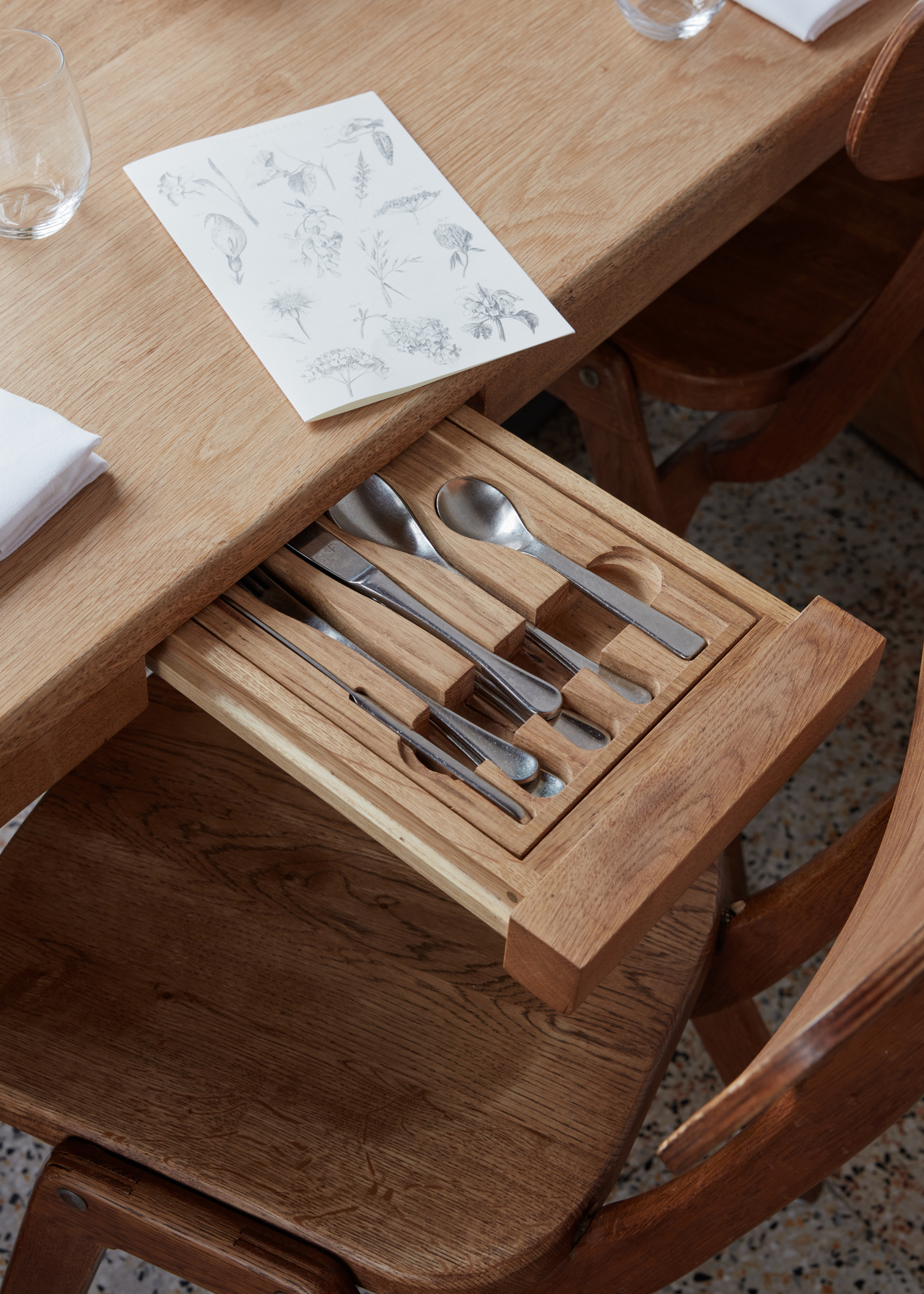 A close-up of a wood dining table with a storage drawer featuring a cutlery insert
