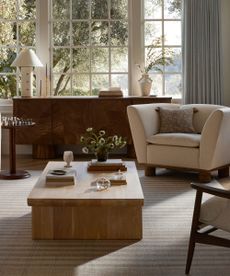 Neutral living room with wood coffee table, striped rug, cream armchair and wood console