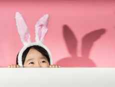 Little girl with rabbit ears headband on a pink background