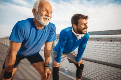 An older man and a middle-aged man pause during a run. They are both fit and attractive.